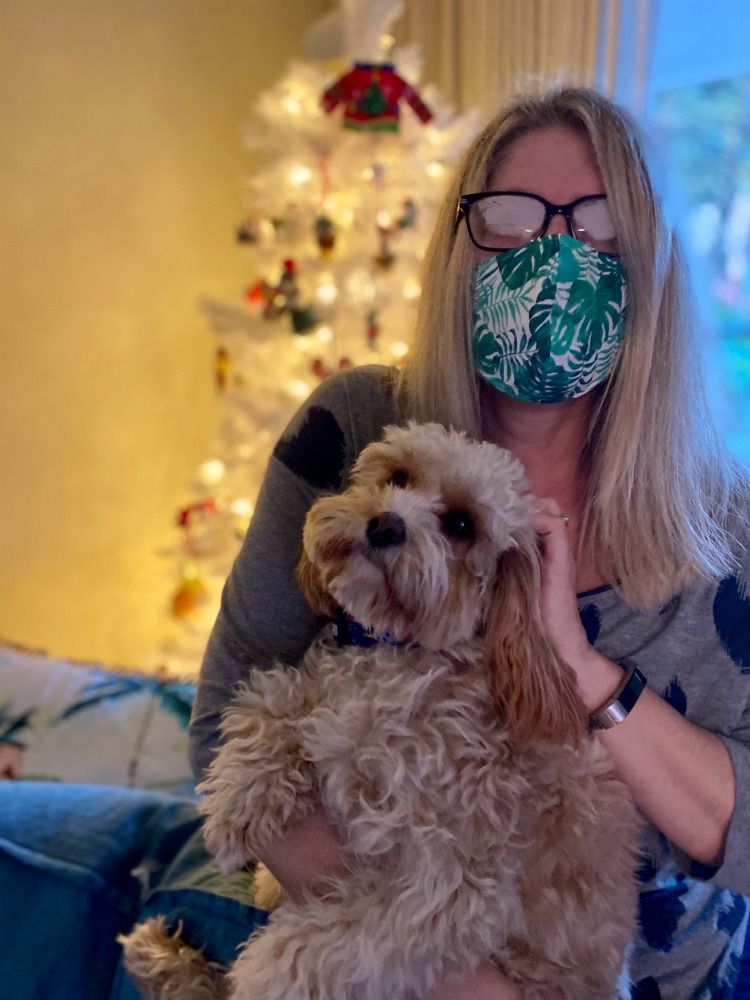 woman wearing a face mask holding a dog in front of a christmas tree