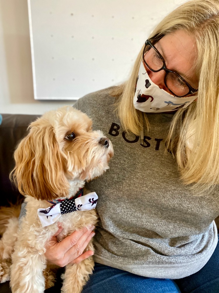 woman wearing mask looking at dog with matching bow