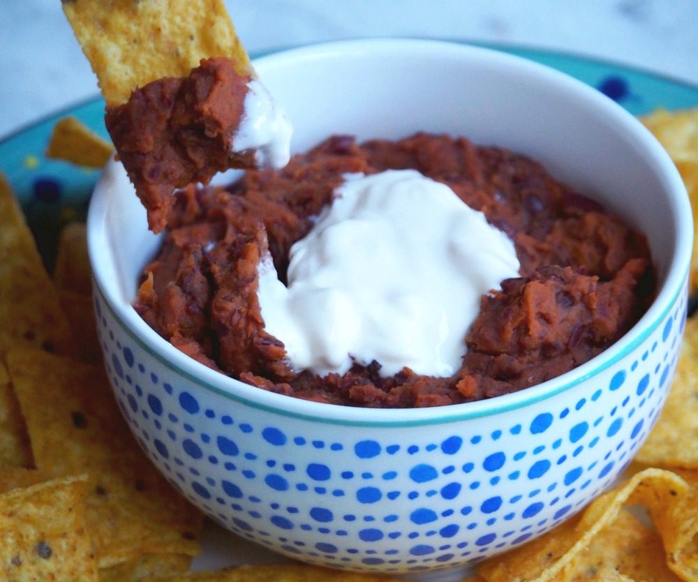 tortilla chip dipped into Mexican bean dip with sour cream
