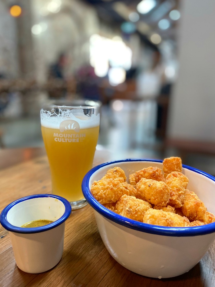 a glass of beer with a bowl of tater tots and curry sauce