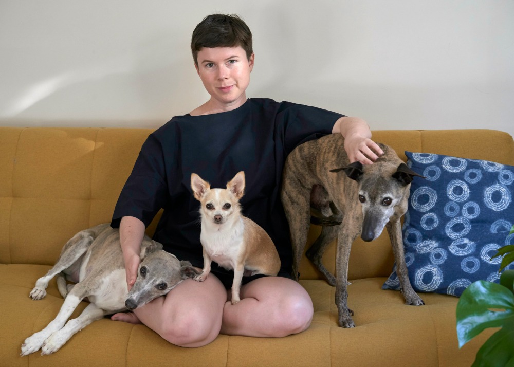 Woman sitting on mustard coloured sofa with one chihuahua and two whippets