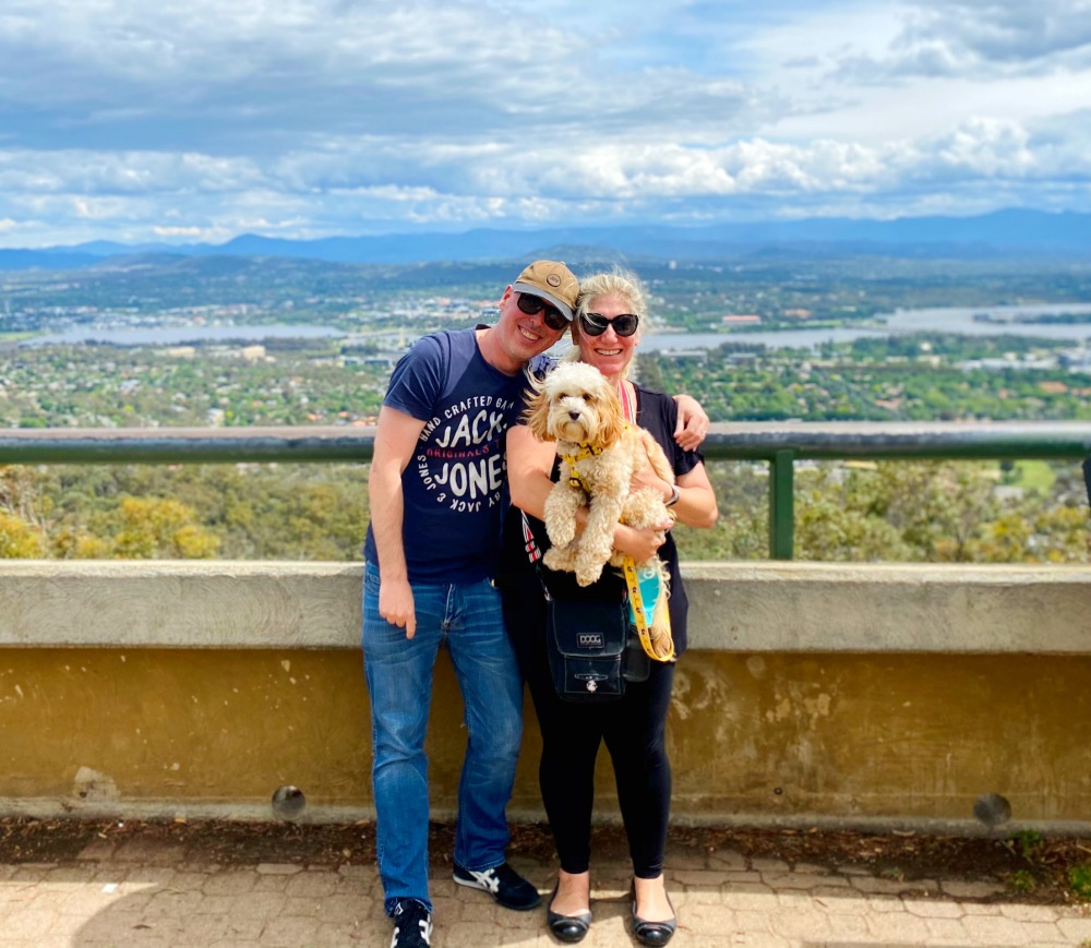 a couple holding a cavoodle at the top of mount ainslie