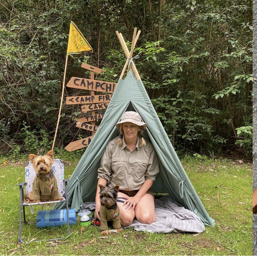 a woman in scout uniform sitting in a teepee with her dog