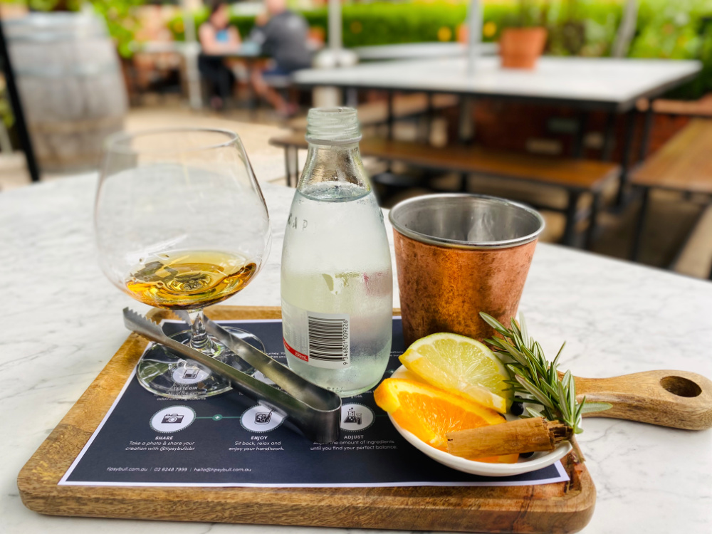 glass of gin tonic water and botanicals on wooden paddle