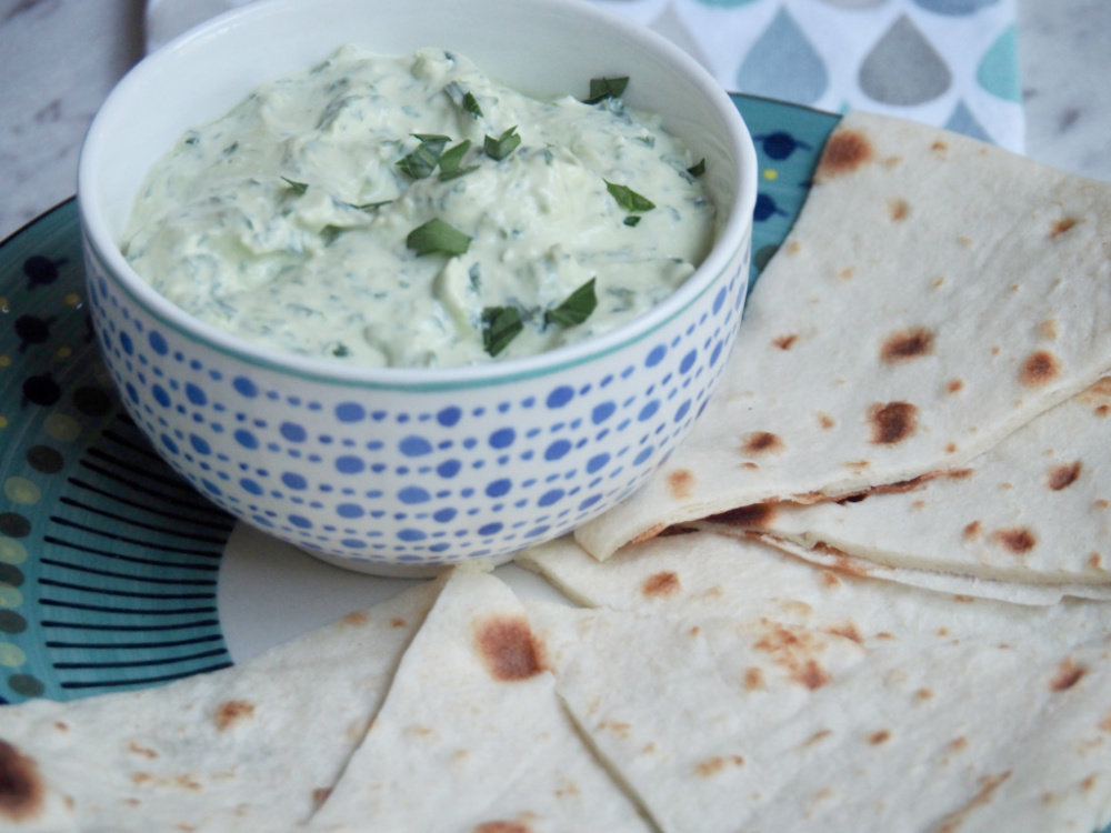 spinach and feta dip in bowl on plate surrounded by flatbread