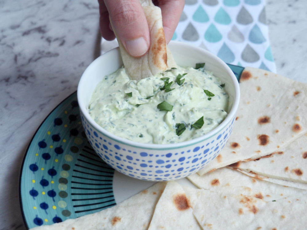 hand dipping some flatbread into bowl of spinach and feta dip