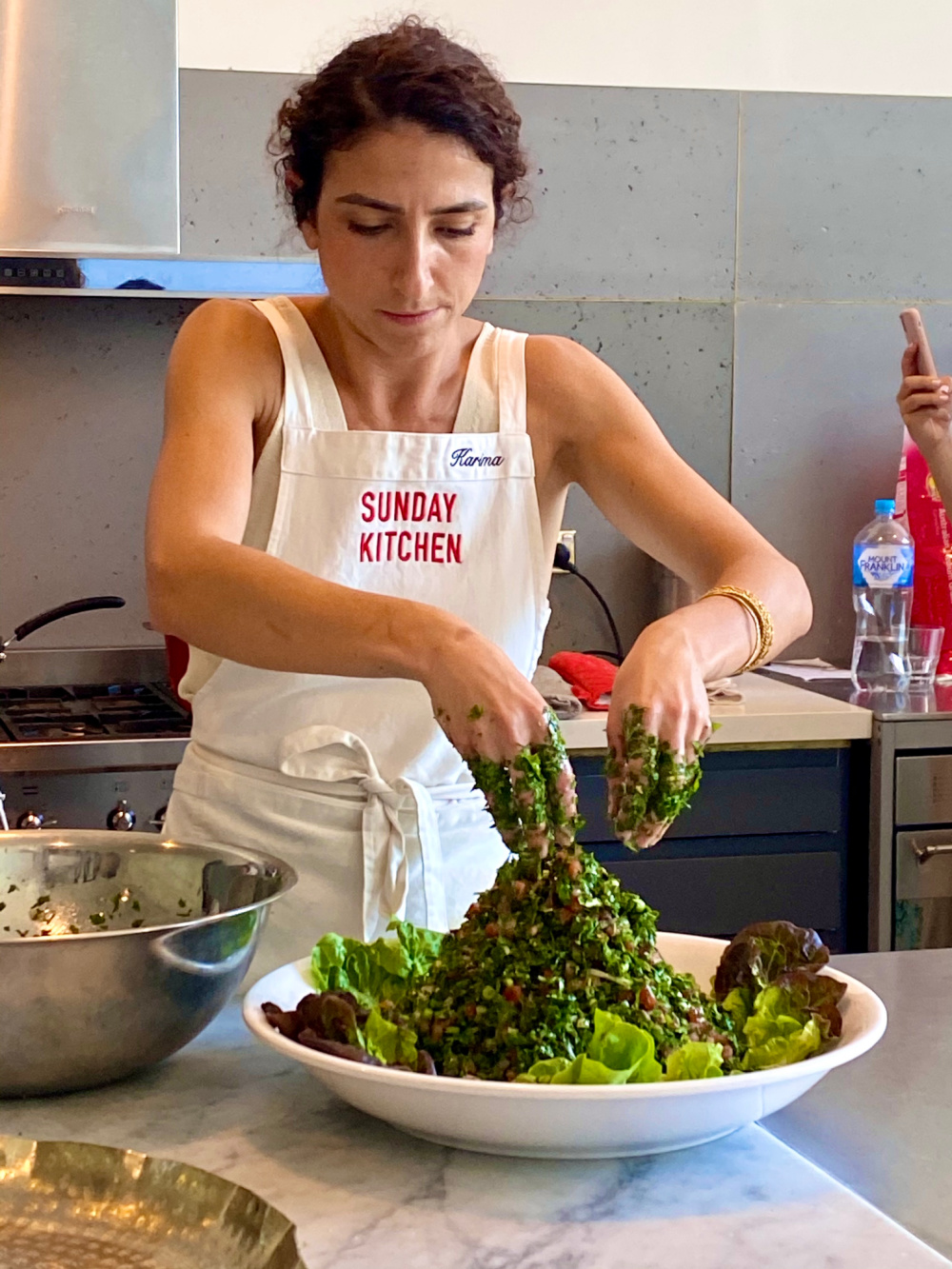 woman using hands to mix a giant bowl of tabbouleh