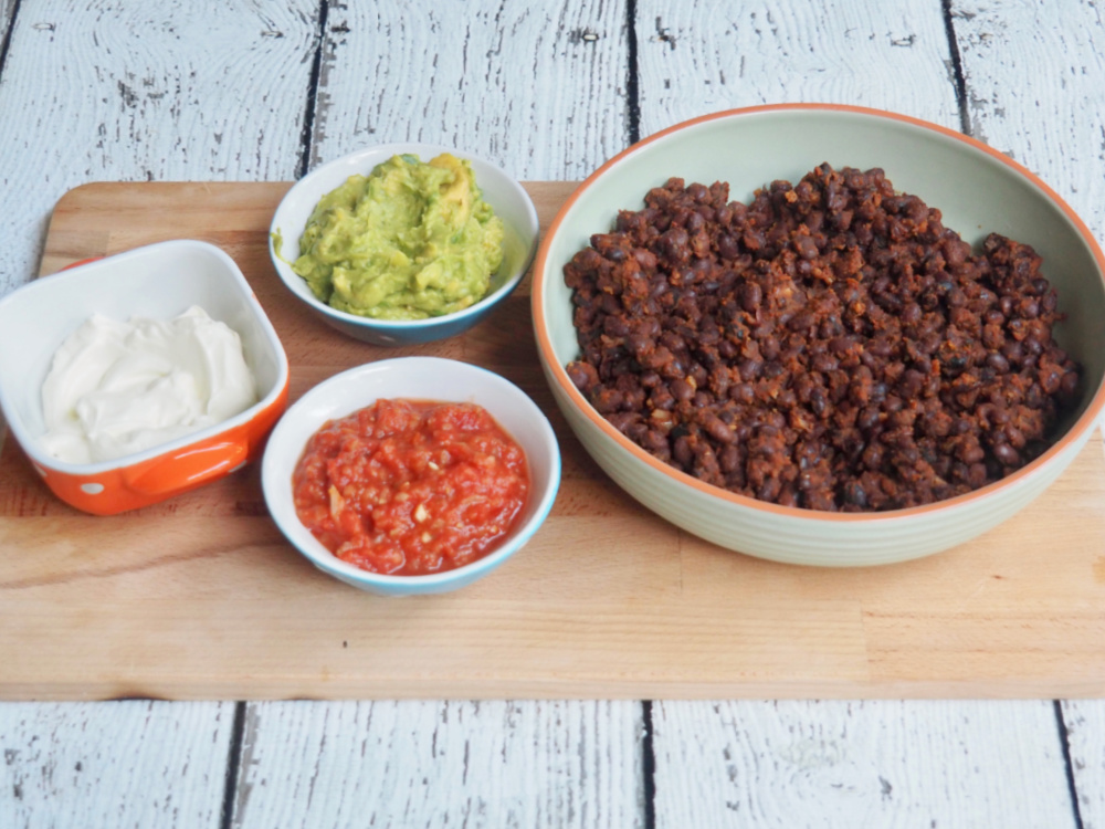 black bean chilli on board with small bowls of sour cream salsa and guacamole
