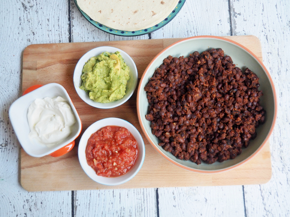 bowl of black bean chilli with small bowls of guacamole and salsa