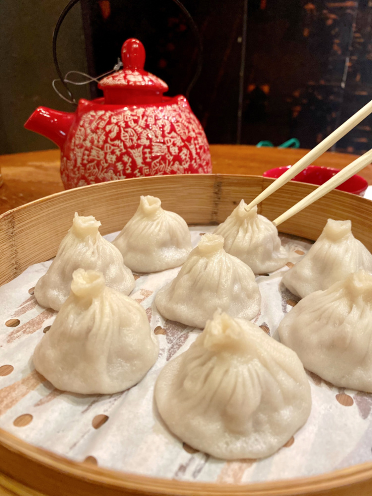 chopsticks picking up a dumpling from a steamer of xiao long bao