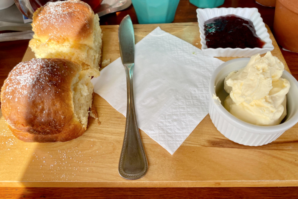 two scones on board with pot of cream and pot of jam