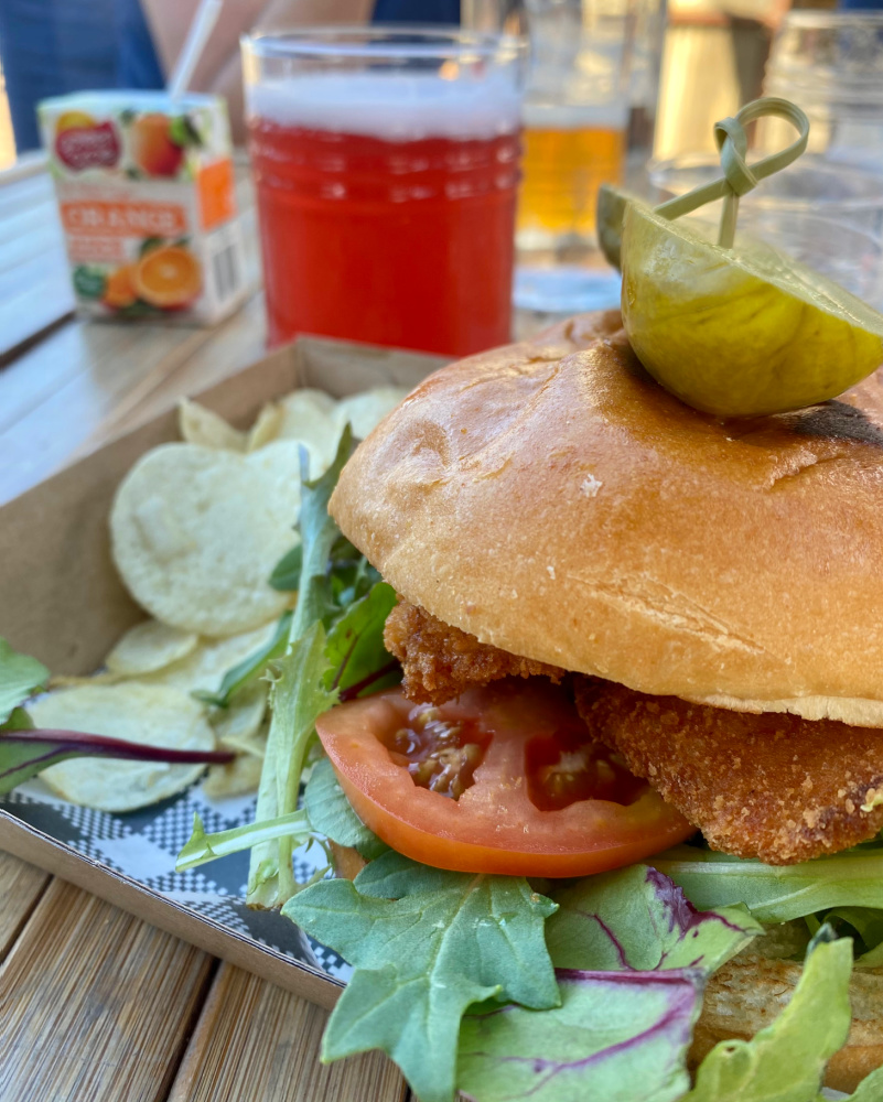 fish burger in bun with beer in background