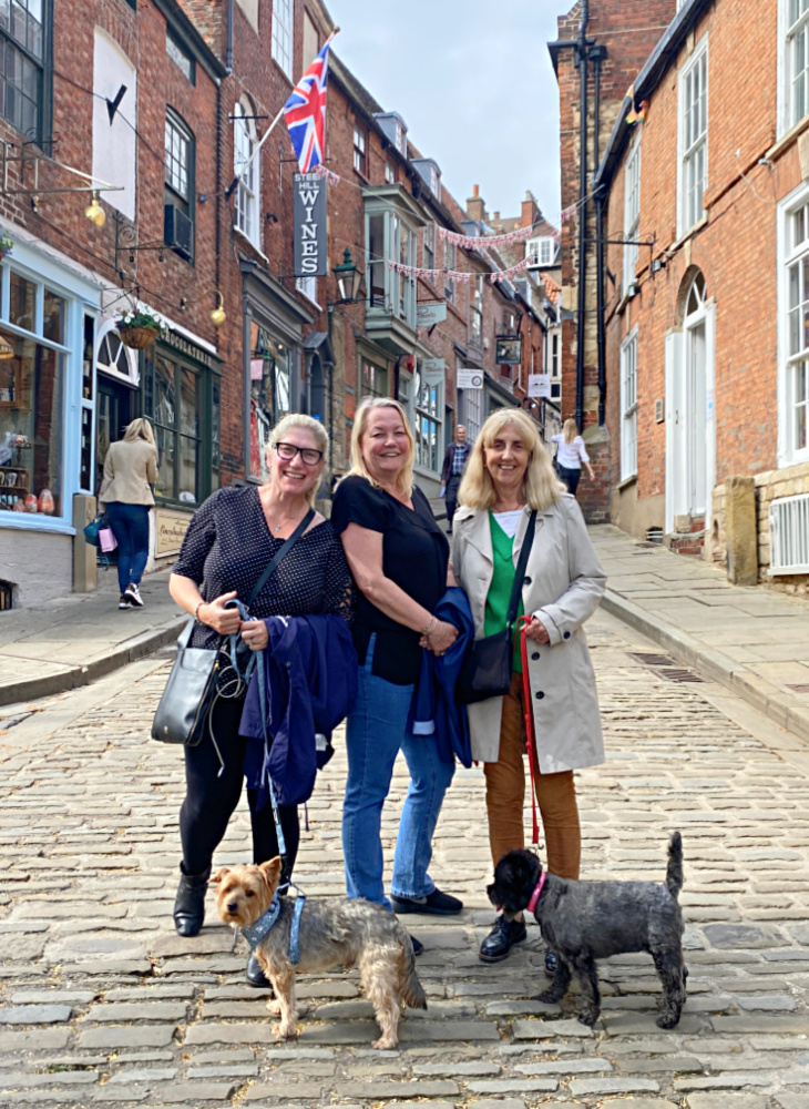 three women standing with 2 dogs at the bottom of an old fashioned steep hill