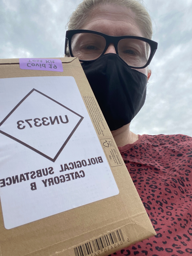 woman wearing a black face mask with a box of home covid test