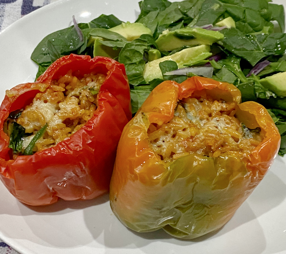 two stuffed peppers on a plate with baby spinach leaves