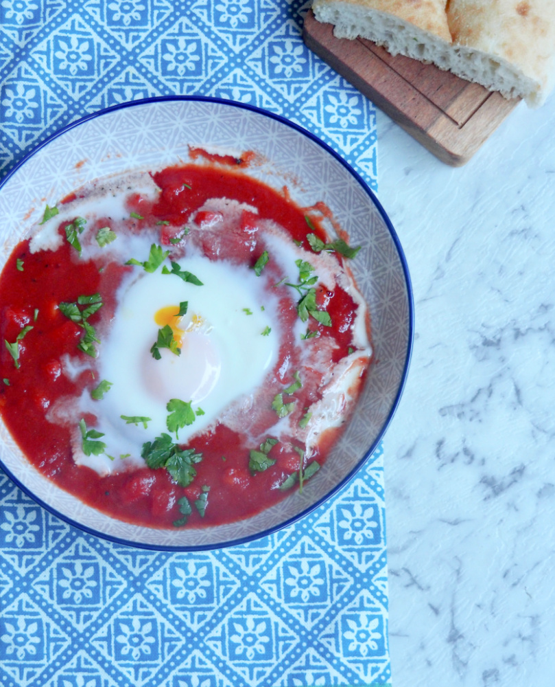 a plate of shakshuka eggs with turkish bread on side