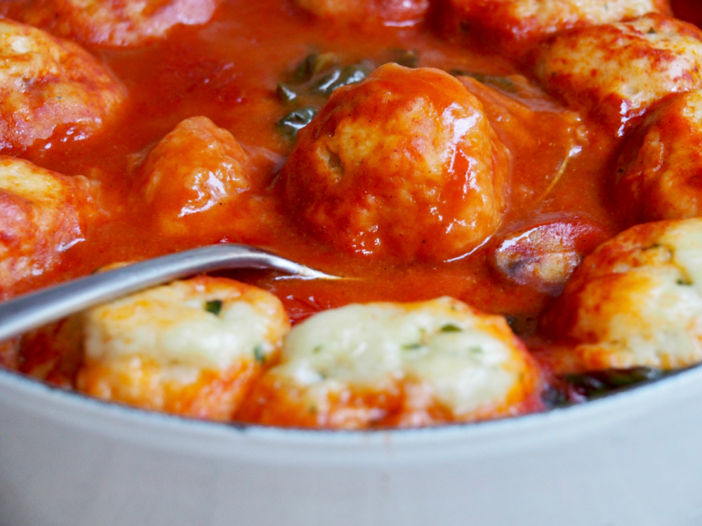 dumpling on serving spoon in pot of chicken and paprika stew