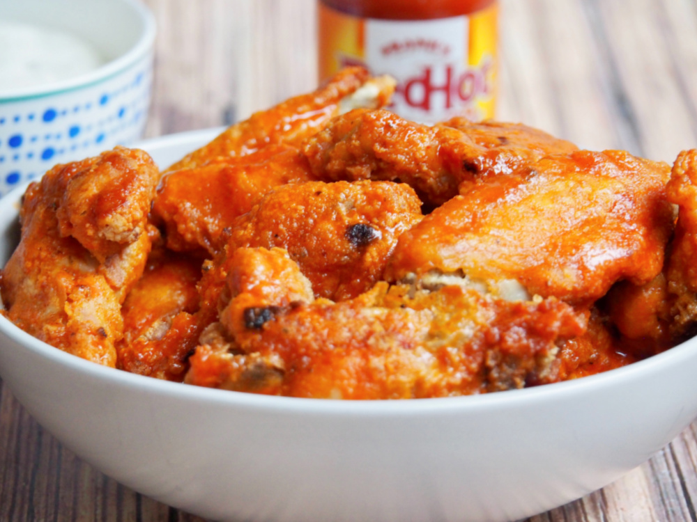 bowl of oven baked chicken wings with Franks hot sauce in the background