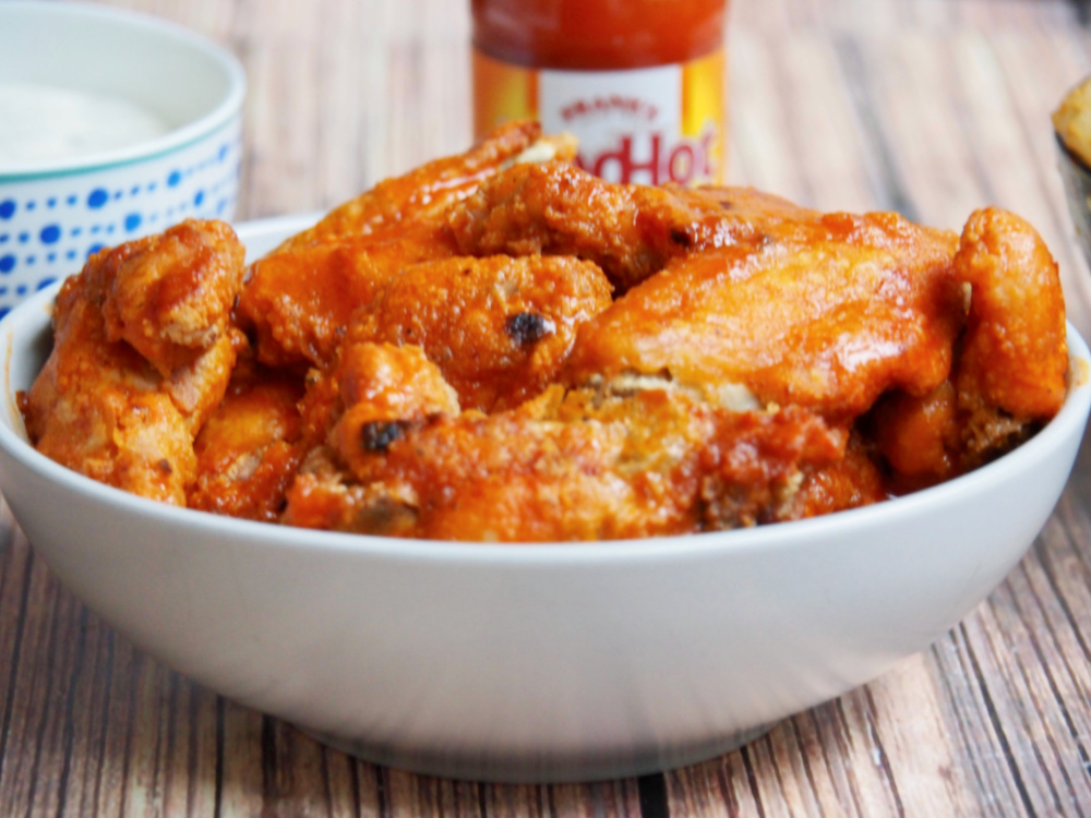 oven baked chicken wings in bowl with Frank's hot sauce in background