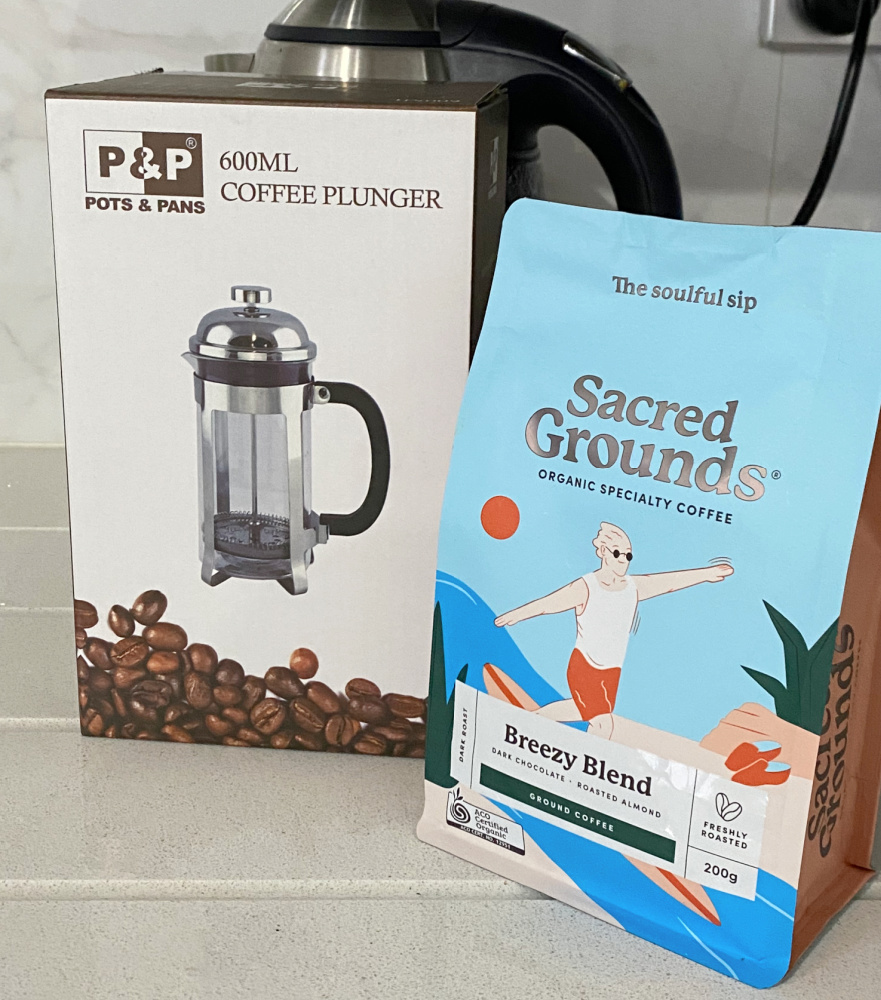 coffee plunger and packet of sacred grounds coffee