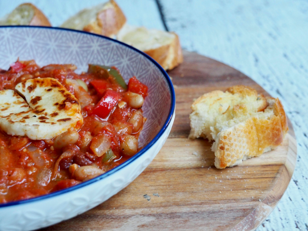 bowl of halloumi and bean stew with a slice of garlic bread with a bite out of it