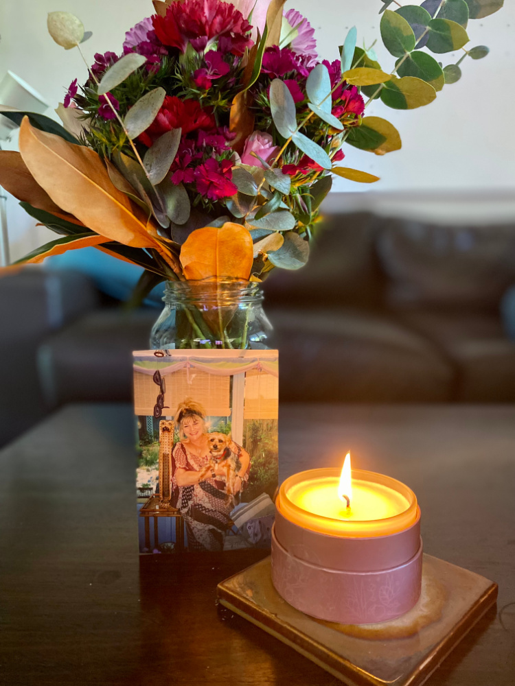 picture of woman holding a dog next to a candle and flowers