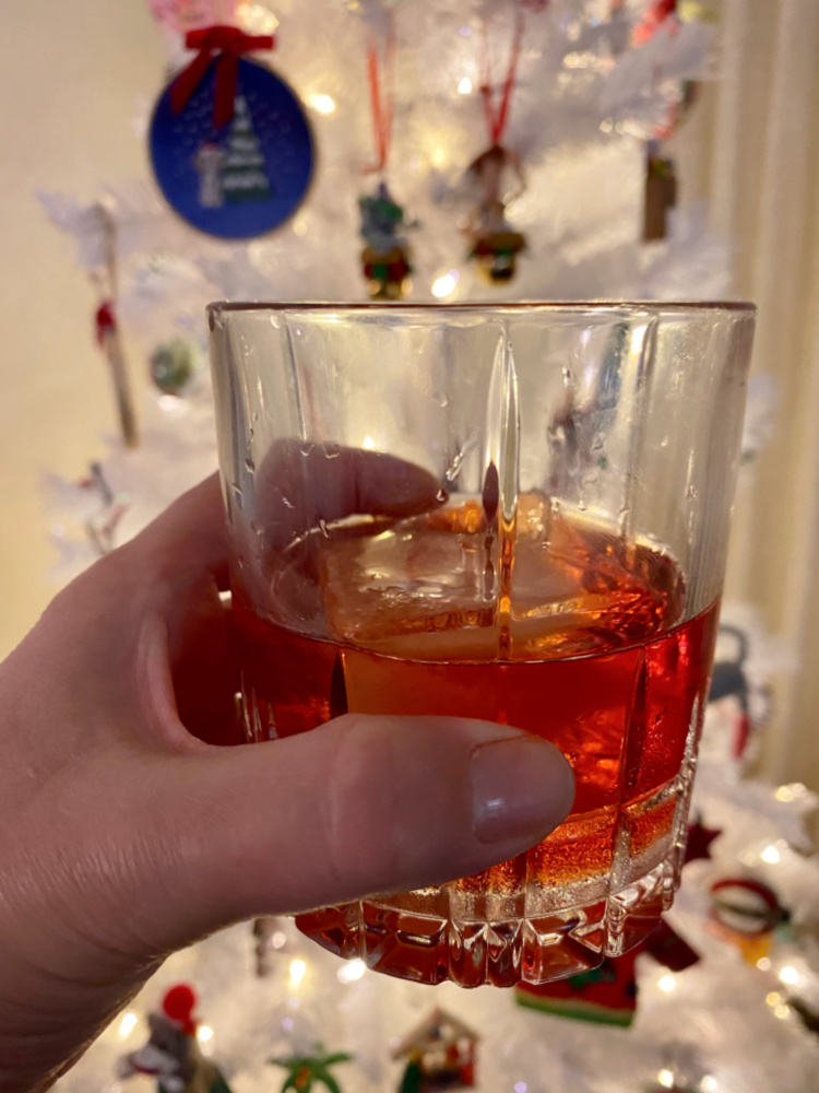 hand holding negroni in front of a white christmas tree