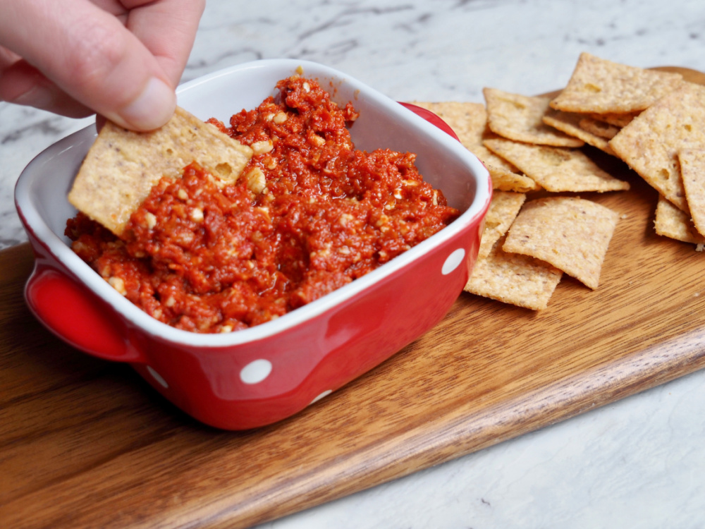 dipping a cracker into sundried tomato pesto