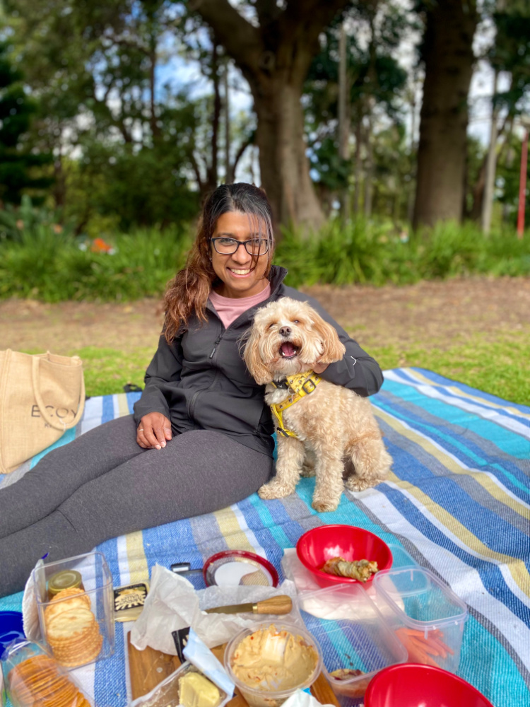 woman sitting on a picnic blanket cuddling a cavoodle