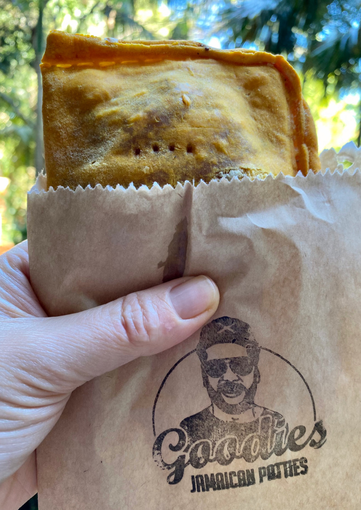 hand holding a Jamaican pattie in a small paper bag