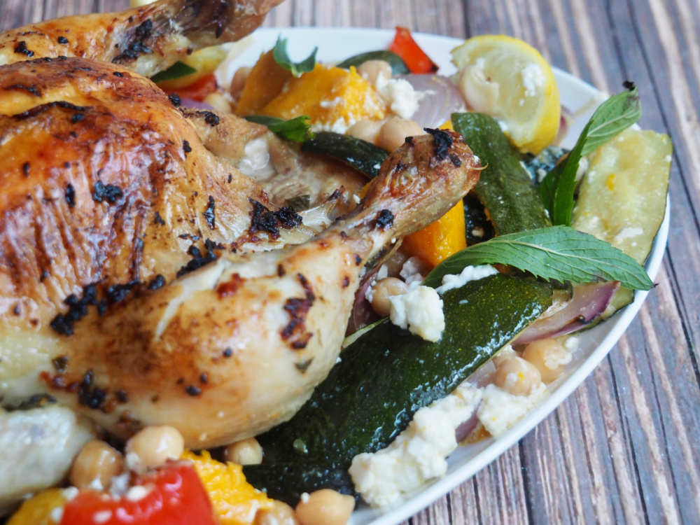 partial close up of roast chicken on white platter with peppers and pumpkin