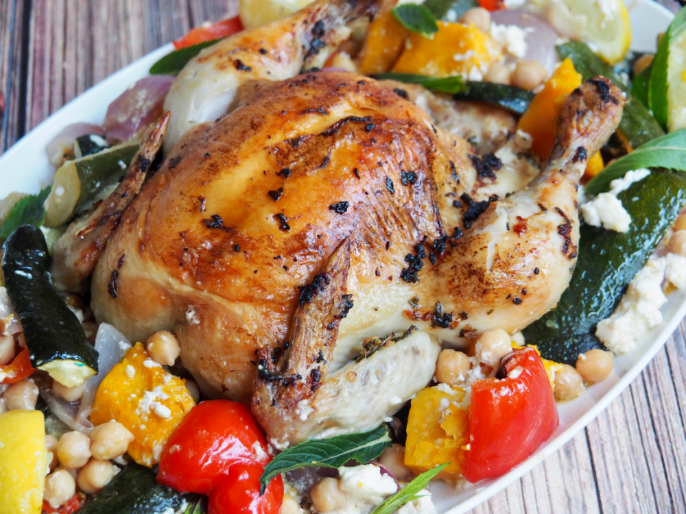 close up of roast chicken surrounded by peppers and pumpkin on white platter