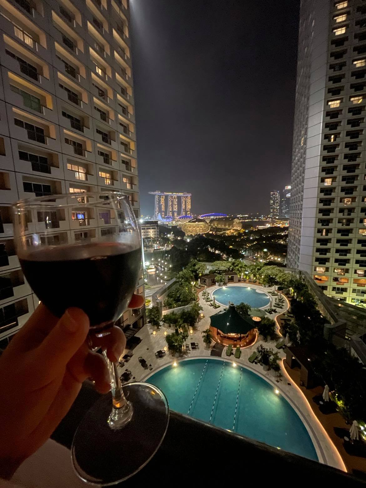 hand holding a glass of wine on balcony overlooking a hotel pool at night