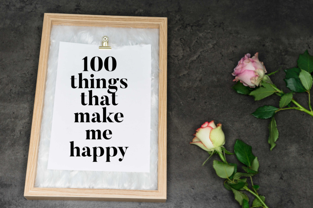 clipboard saying 100 things that make me happy on black background next to two pink roses