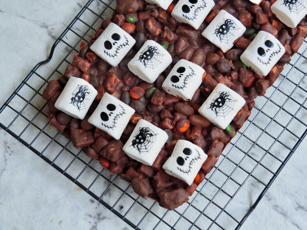 slab of halloween rocky road topped with white marshmallows decorated with skulls and spiders