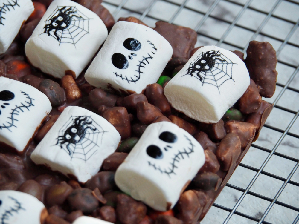 uncut rocky road topped with marshmallows decorated with skull faces and spiders