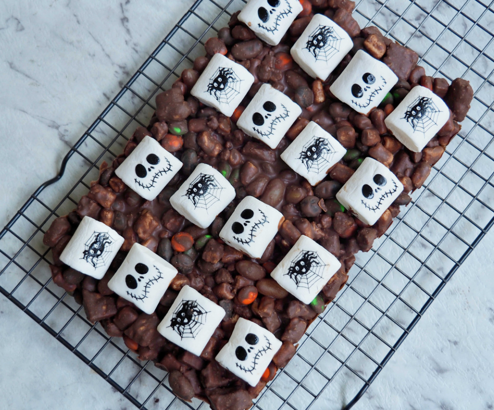 slab of uncut halloween rocky road topped with marshmallows decorated with skull faces and spiders