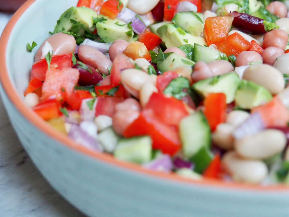 mixed bean salad in large shallow dish with chopped tomato cucumber avocado and red onion