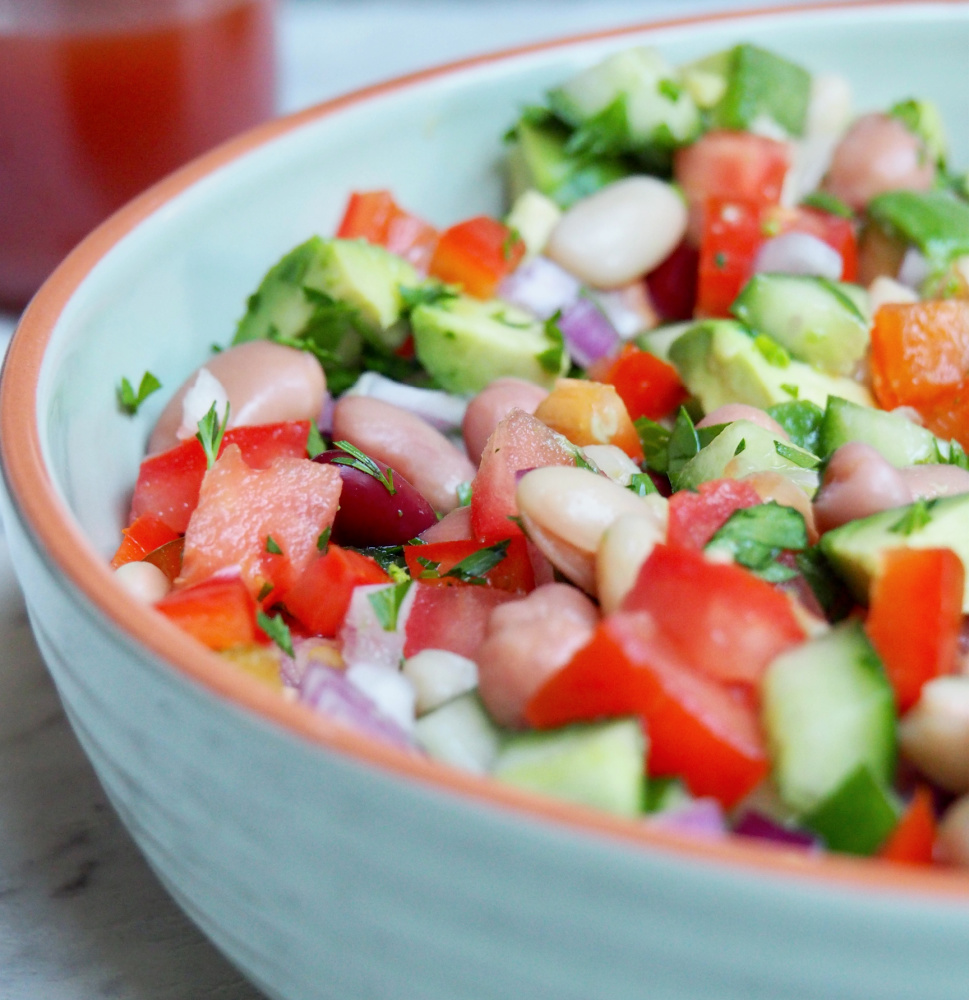 light green dish full of mixed bean salad with chopped tomatoes avocado cucumber red onion and mixed beans