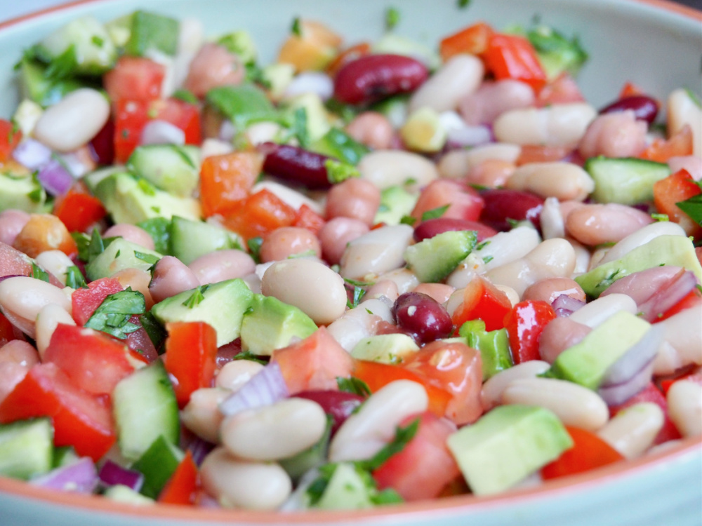 salad  bowl full of mixed beans and chopped tomato avocado cucumber and red onion
