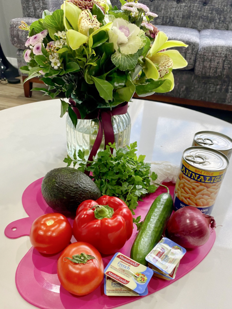 vase of flowers and pink apple shaped chopping board with ingredients for mixed bean salad