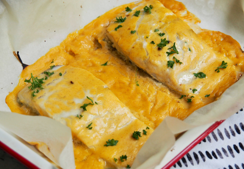 2 fish fillets in baking dish covered in orange and mustard sauce and garnished with fresh parsley