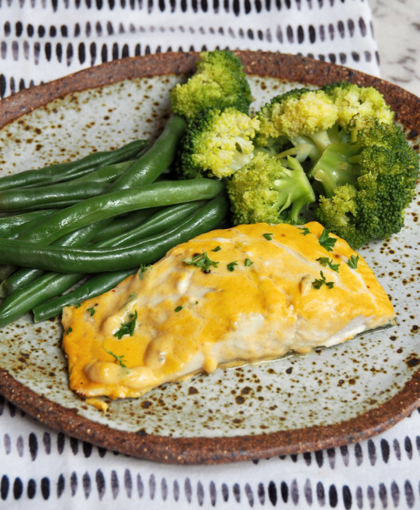 fish fillet covered in orange and mustard sauce with green beans and broccoli in the background