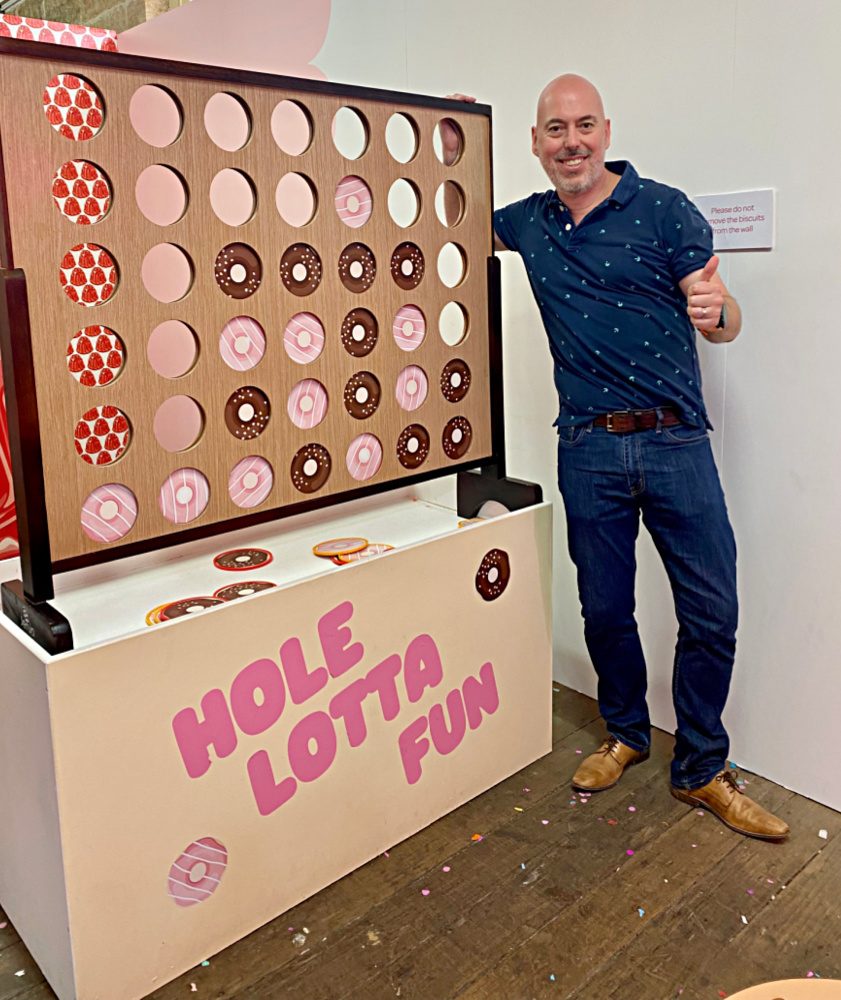 man doing a thumbs up next to a giant donut connect 4