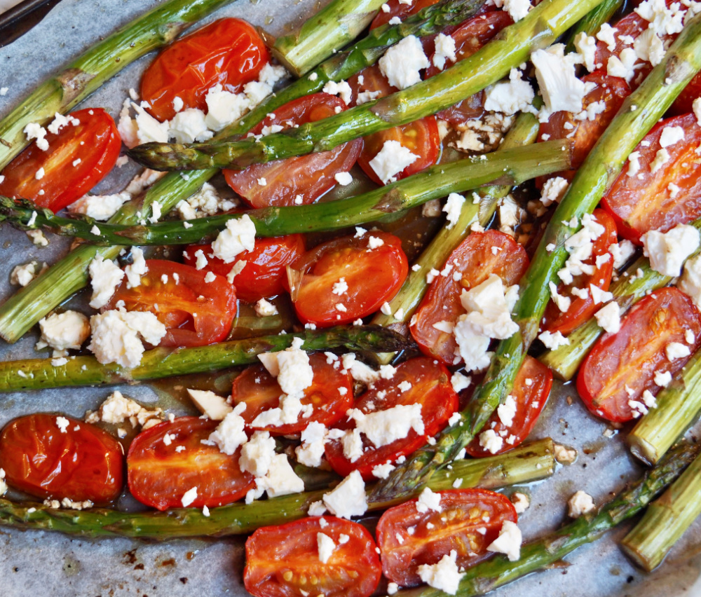 baking sheet lined with baking paper and topped with roasted asparagus spears halved cherry tomatoes and topped with crumbled feta