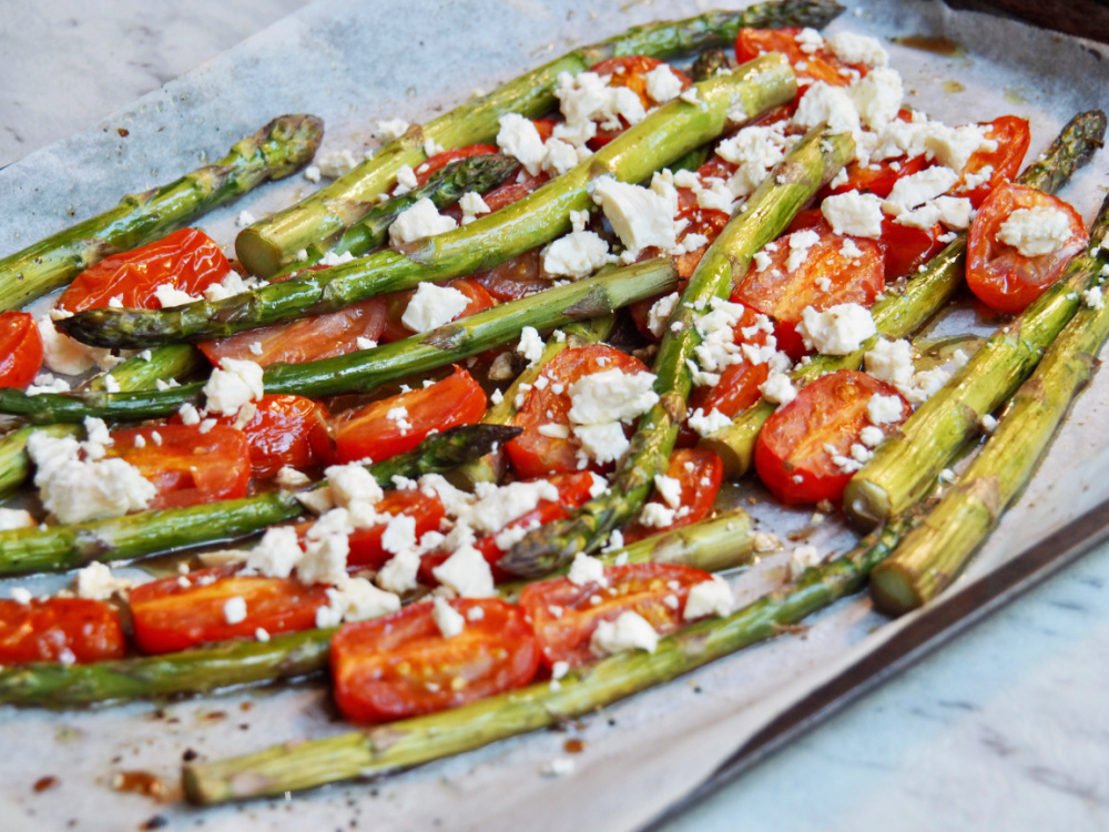baking sheet lined with baking paper and topped with roasted asparagus spears halved cherry tomatoes and topped with crumbled feta