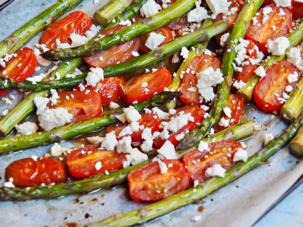 baking sheet lined with baking paper and topped with roasted asparagus spears halved cherry tomatoes and topped with crumbled feta