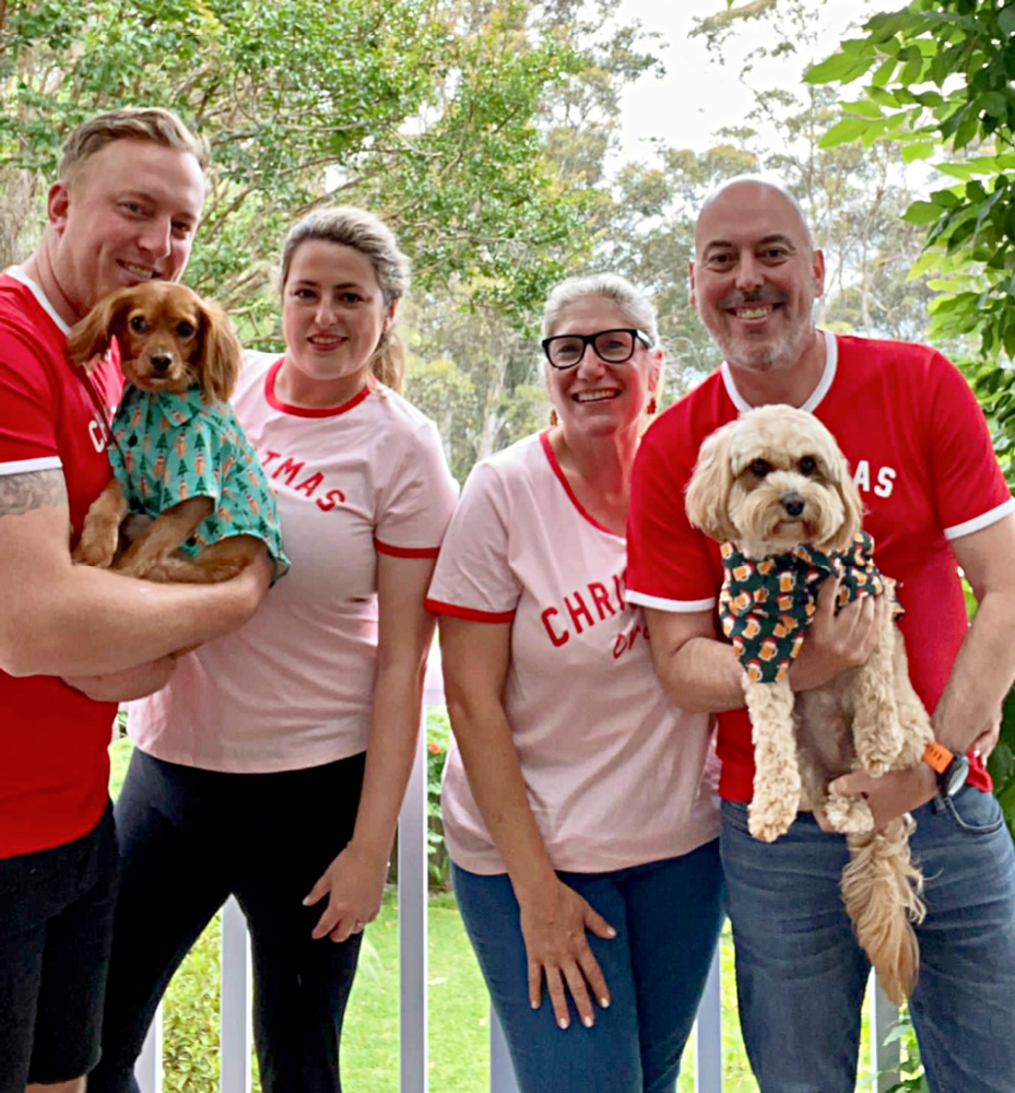 2 couples wearing matching tees saying Christmas crew. Each of the  men is holding a cavoodle