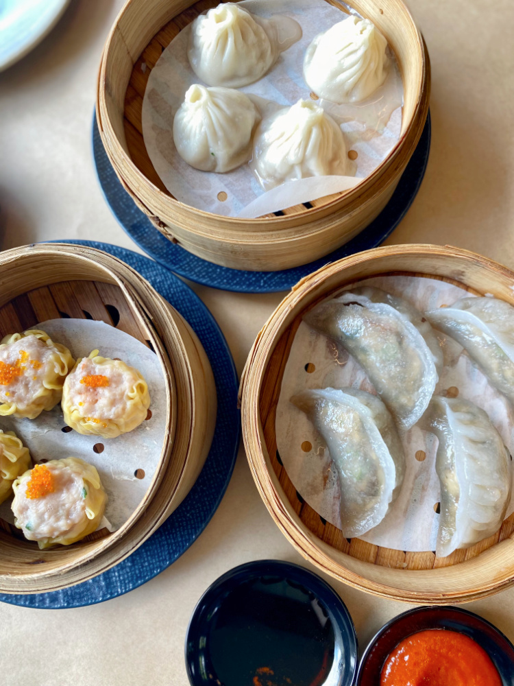 three bamboo steamers each filled with a different dumpling