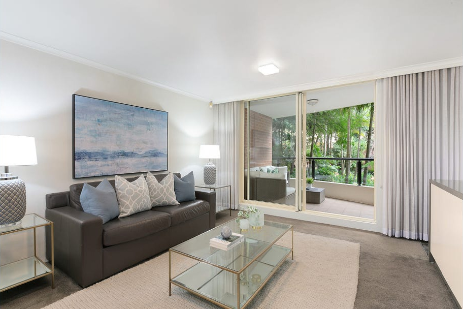 living room with brown sofa along back wall with white rug and glass coffee table in centre